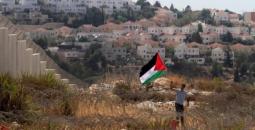 شاب يحمل علم فلسطين قبالة مستوطنة إسرائيلية في الضفة الغربية.jpg